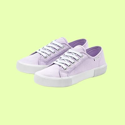 Lavendelfarbene Sneaker mit weißen Schnürsenkeln auf hellgrünem Hintergrund.