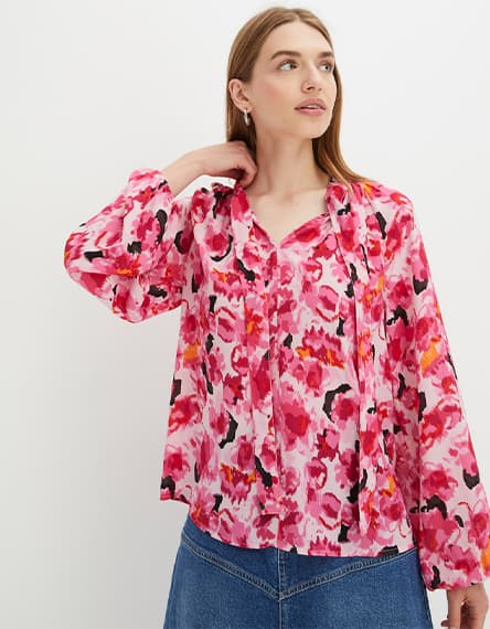 Frau trägt pink-gemusterte Bluse mit V-Ausschnitt und Jeansrock.