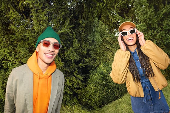 Zwei Personen in farbiger Freizeitkleidung posieren im Grünen vor dichten Büschen