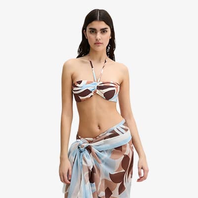 Frau im gemusterten Bikini mit passendem Pareo steht frontal und blickt in die Kamera