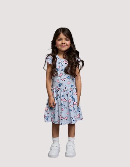 Kind in hellblauem Kleid mit buntem Muster steht frontal und trägt weiße Sneaker